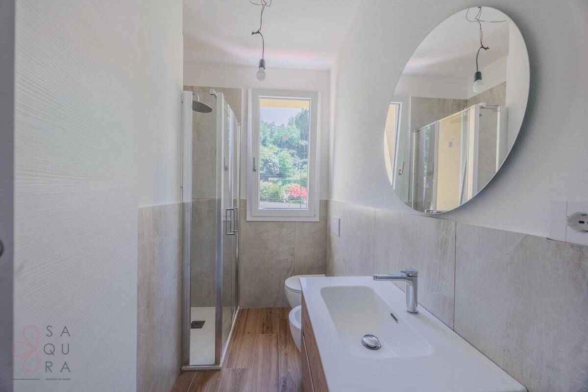 Modernes Badezimmer mit Dusche, Einzelwaschbecken und Fenster mit Blick ins Grüne.