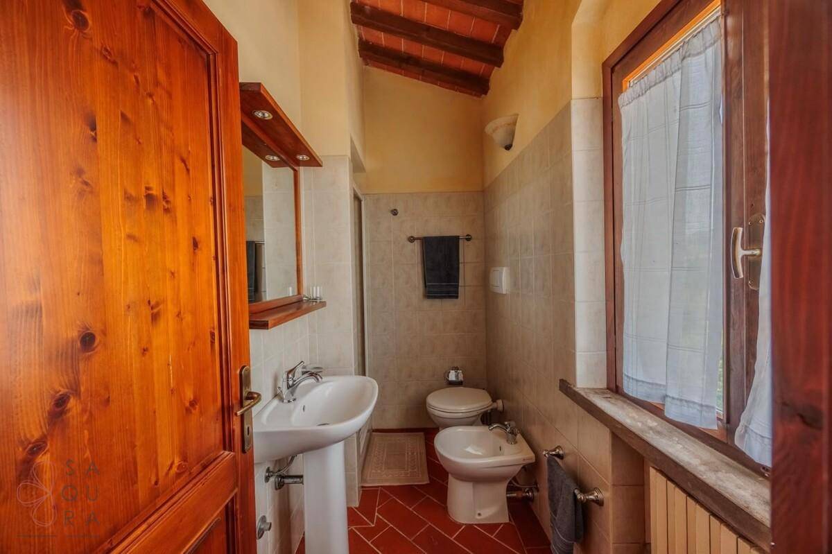 Badezimmer mit Waschtisch, WC, Bidet, gefliesten Wänden und Terrakottaboden.