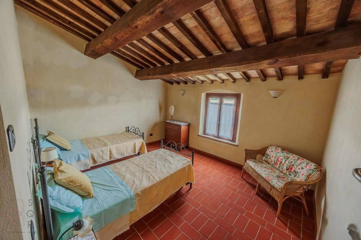 Schlafzimmer mit zwei Einzelbetten, Terrakottaboden und sichtbaren Holzbalken an der Decke.