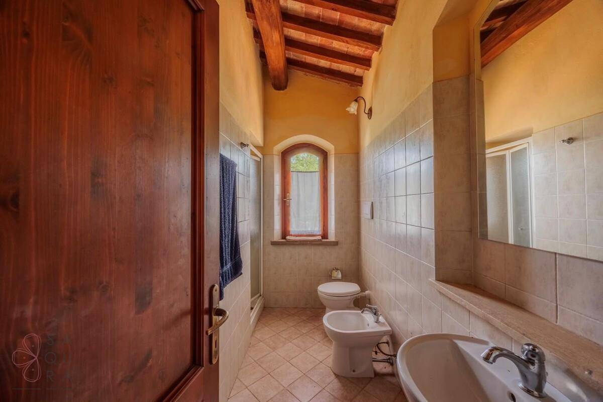 Badezimmer mit Waschtisch, WC, Bidet, gefliesten Wänden und Holzbalkendecke.