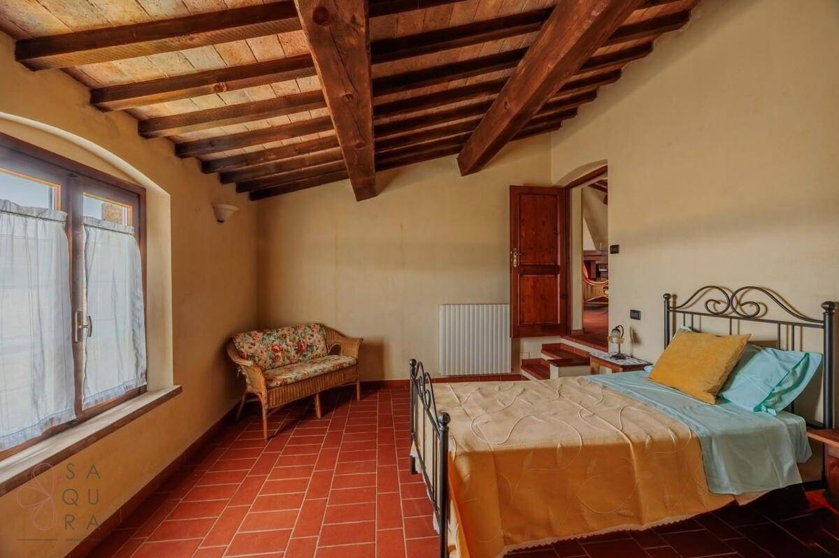 Helles Schlafzimmer mit Terrakottaboden, Holzbalkendecke und Blick ins Grüne.