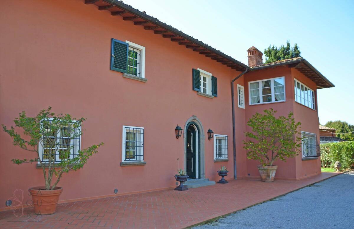 Traditionelles Landhaus mit ockerfarbener Fassade, grünen Fensterläden und gepflastertem Eingangsbereich.