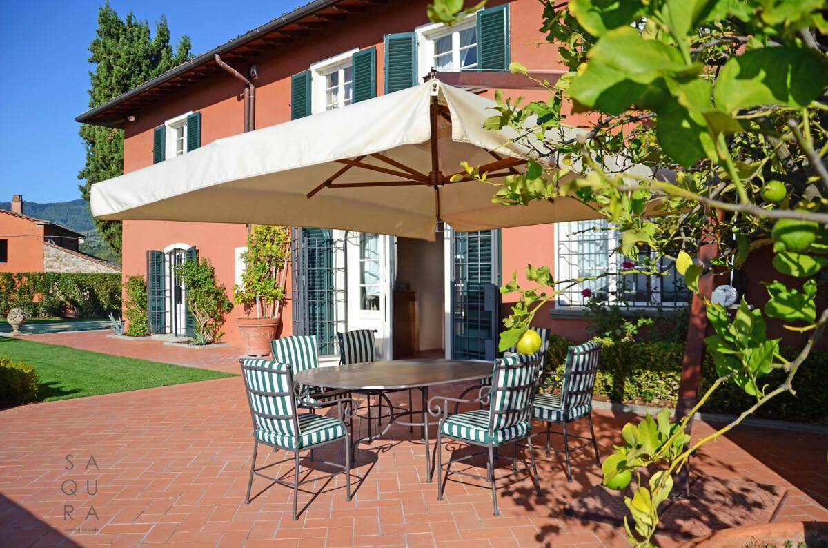 Gemütliche Terrasse mit Esstisch, Stühlen und großem Sonnenschirm vor dem Landhaus.