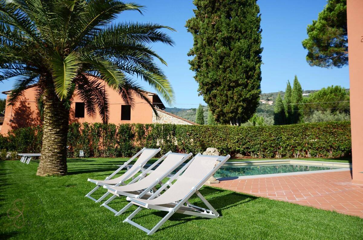 Entspannender Poolbereich mit Sonnenliegen und Palmen, umgeben von einem grünen Garten.