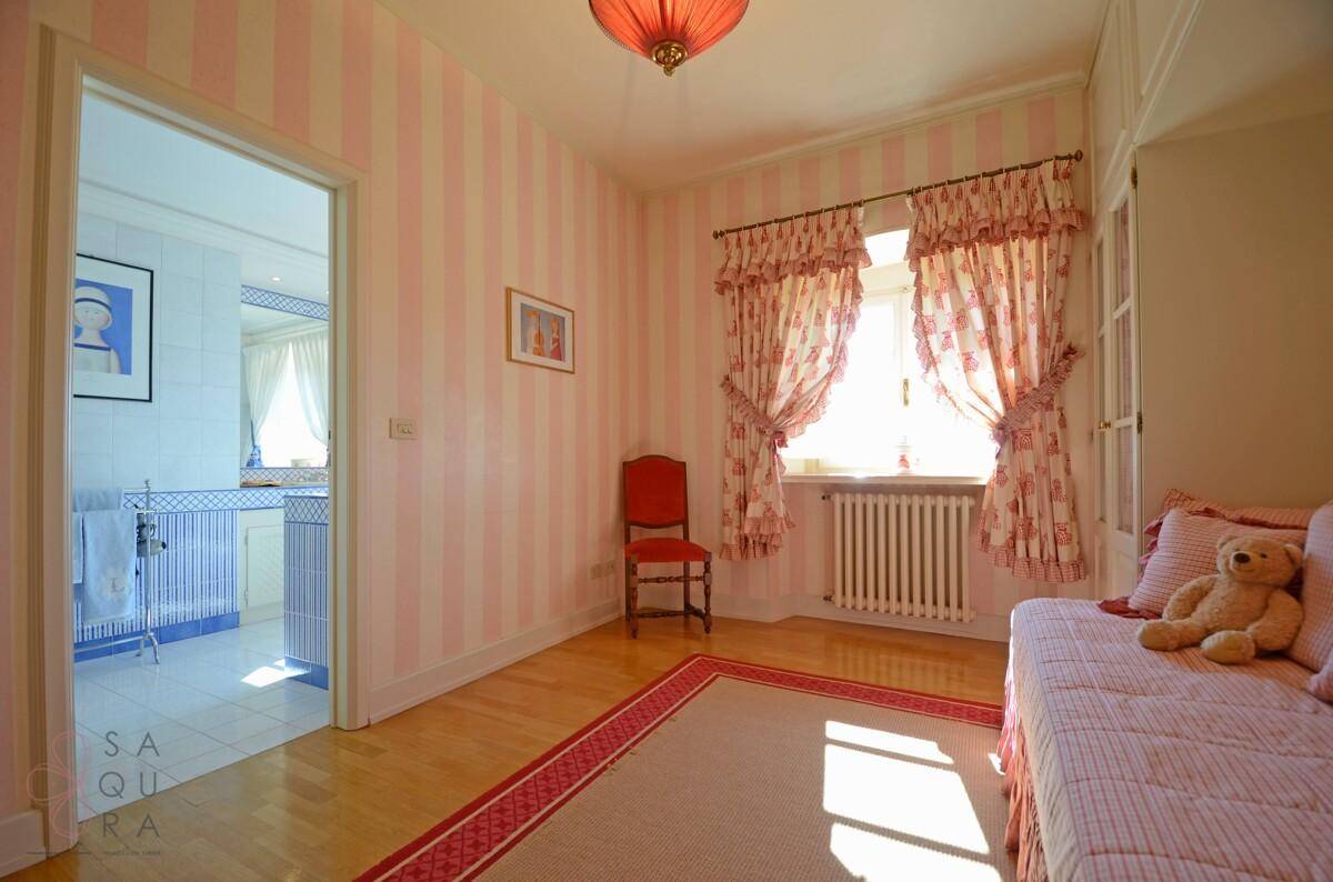 Mädchenzimmer mit rosa gestreiften Tapeten, Holzboden und Zugang zum Badezimmer.