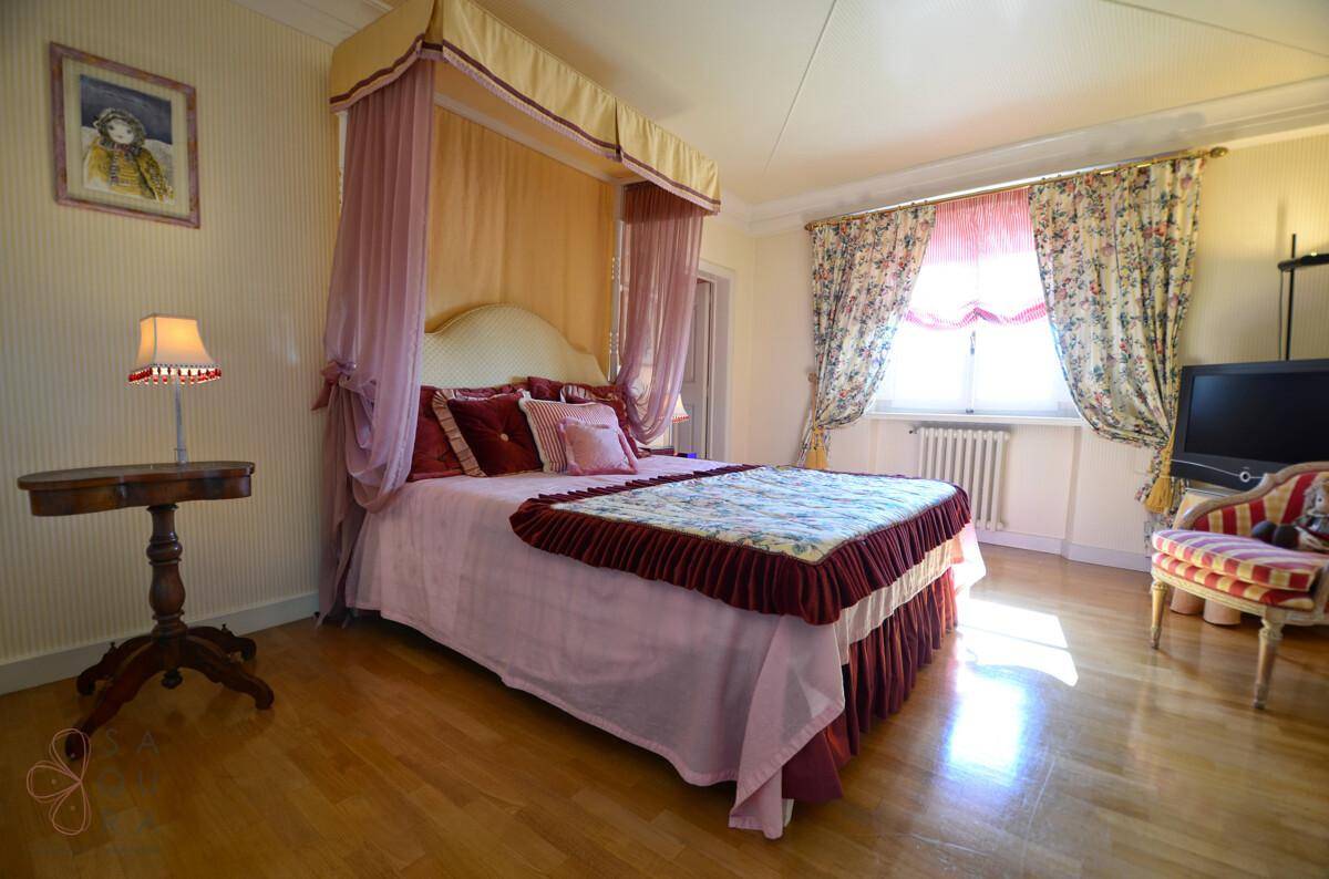 Romantisches Schlafzimmer mit Himmelbett, Holzboden und floralen Vorhängen.