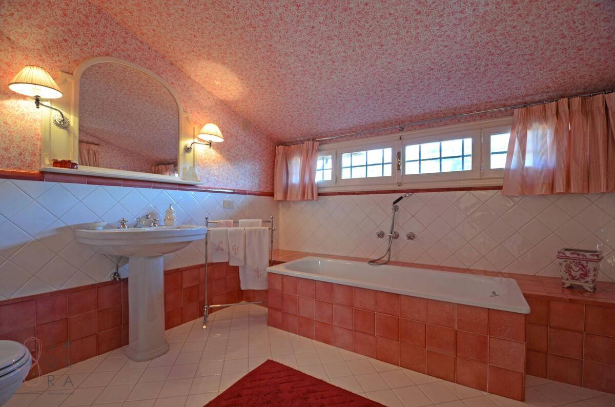 Badezimmer mit Badewanne, Waschtisch und rosa Fliesen unter Dachschräge.