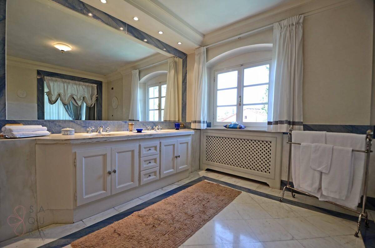 Geräumiges Badezimmer mit Doppelwaschbecken, Marmoroberflächen und großen Fenstern.