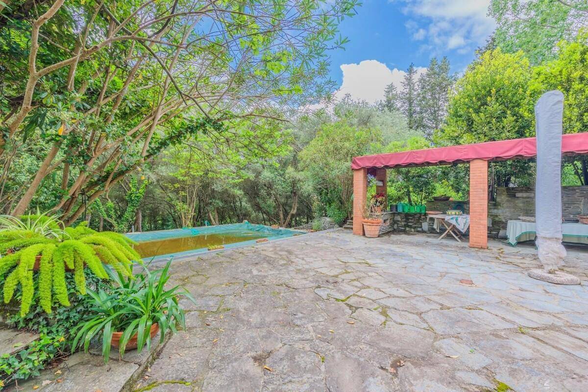 Außenbereich mit Pool, großer Steinterrasse und einer überdachten Pergola, umgeben von viel Grün.