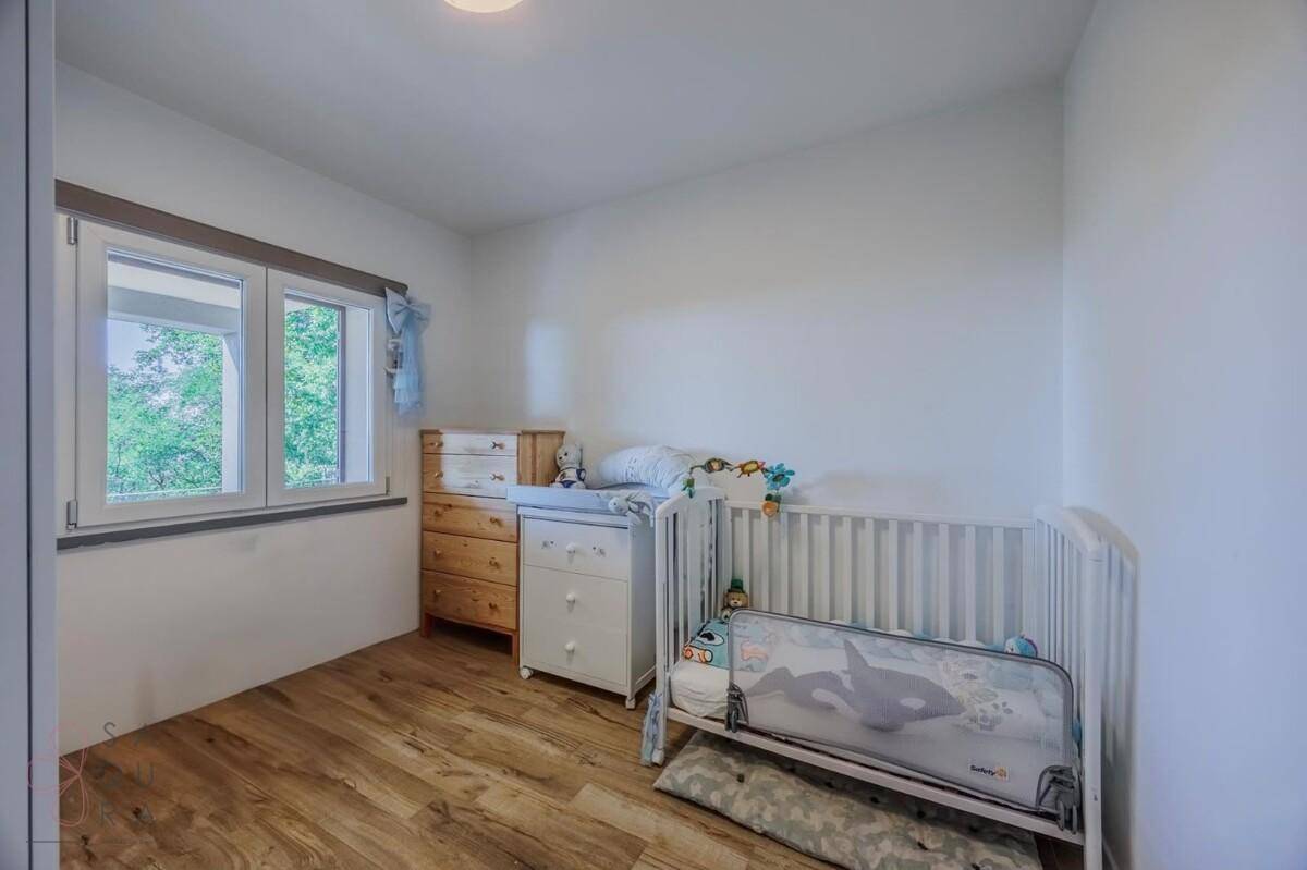 Helles Kinderzimmer mit Holzboden, Babybett und Fenster mit Ausblick.