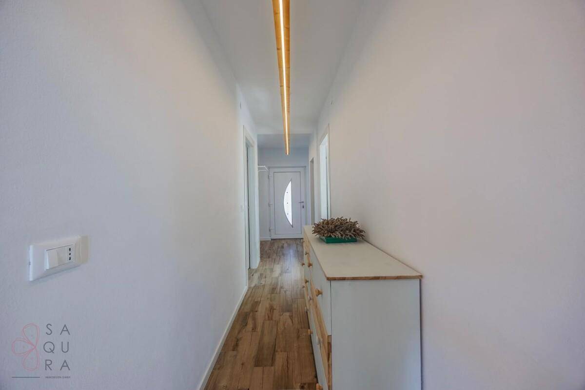 Langer, heller Flur mit Holzboden und moderner Deckenbeleuchtung.
