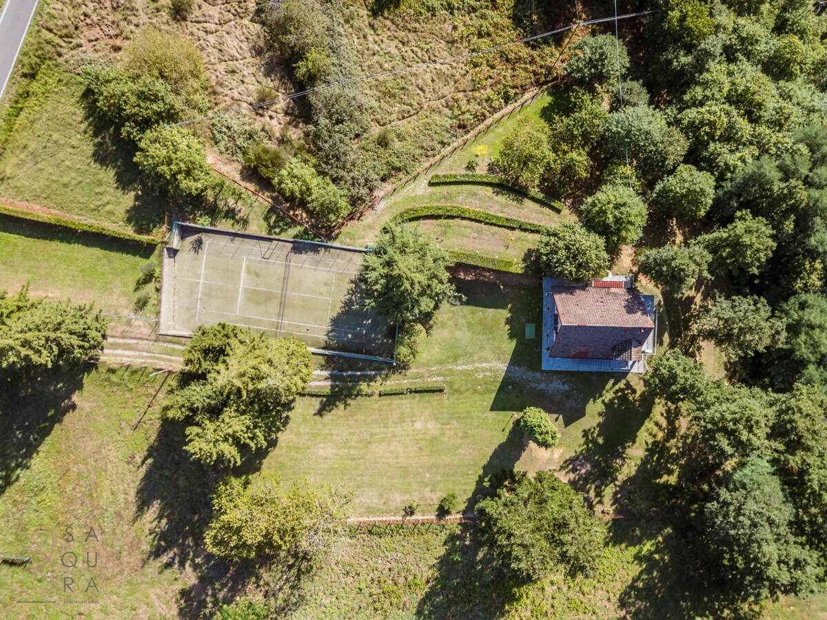 Luftaufnahme des Anwesens mit eigenem Tennisplatz, umgeben von üppiger Natur.