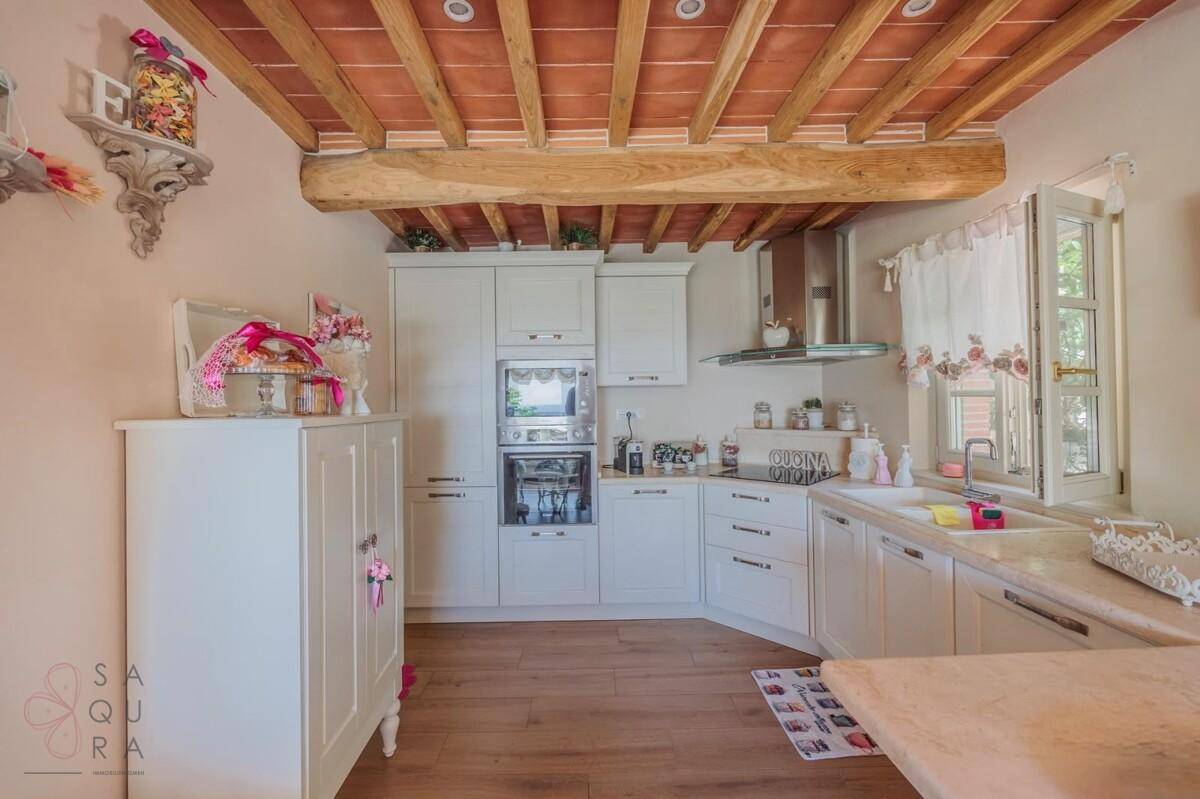 Helle Küche mit weißen Einbauschränken, Holztheke und traditionellen Deckenbalken.