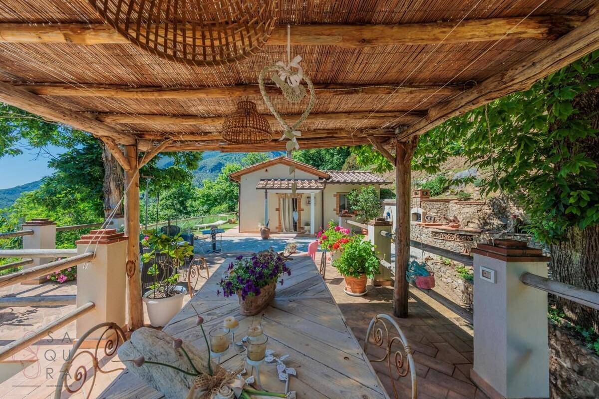 Überdachte Terrasse mit rustikalem Holztisch und Blick auf die umliegende grüne Hügellandschaft.