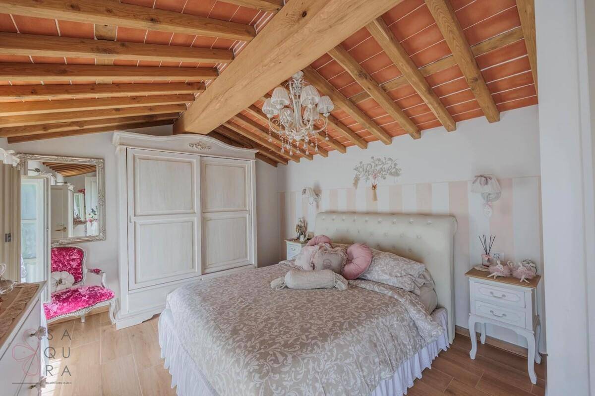 Romantisches Schlafzimmer mit Holzbalkendecke, weißem Kleiderschrank und elegantem Doppelbett.