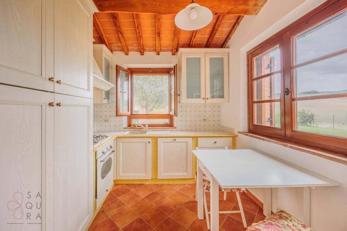 Helle Küche im Landhausstil mit Terrakottaboden, Holzbalkendecke und Blick ins Grüne.