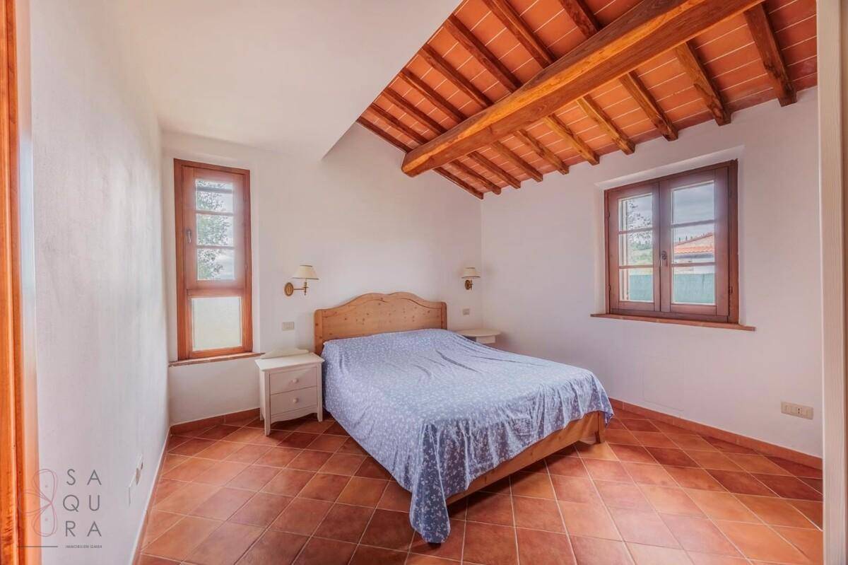 Helles Schlafzimmer mit Doppelbett, Terrakottaboden und Holzbalkendecke mit zwei Fenstern.