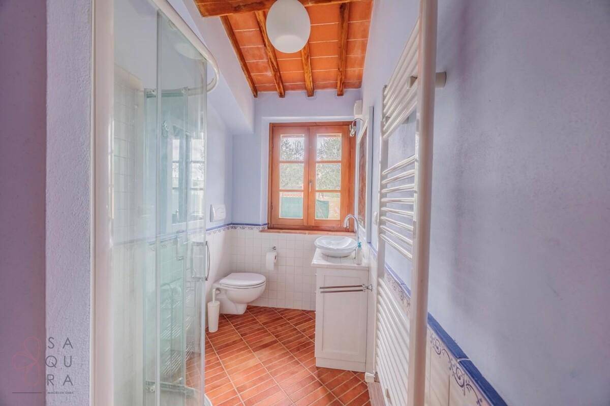Badezimmer mit Dusche, Terrakottaboden, Holzbalkendecke und beheiztem Handtuchhalter.