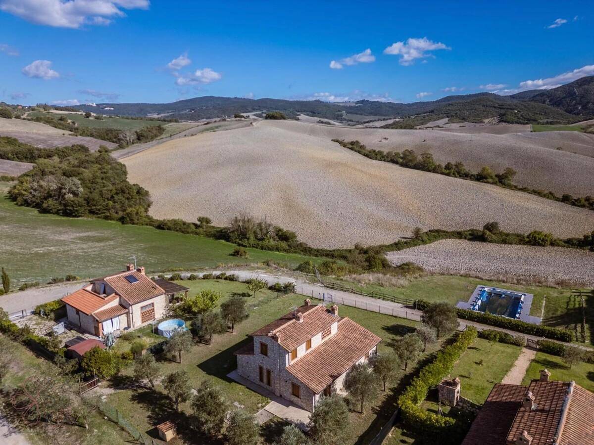 Luftaufnahme eines Anwesens mit mehreren Steinhäusern, Pool und weiten Feldern in hügeliger Landschaft.