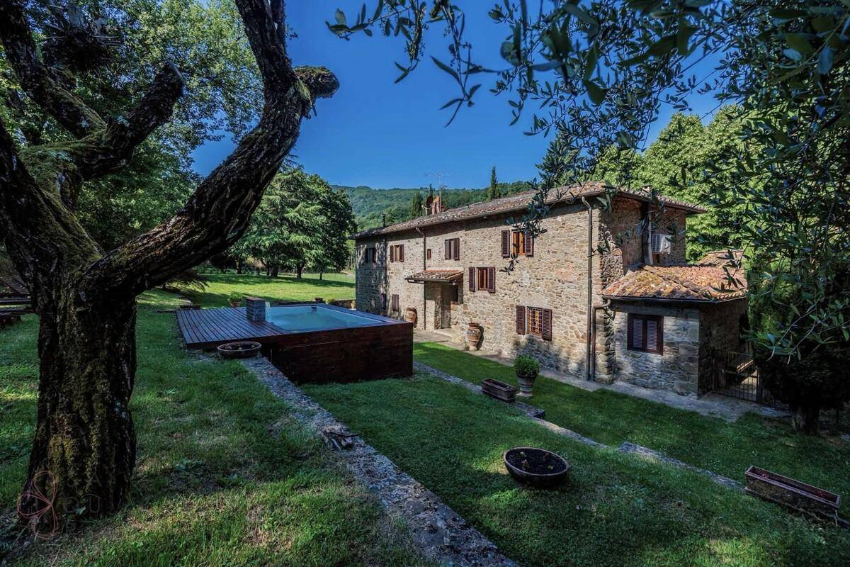 Malerisches Steinhaus umgeben von einem grünen Garten mit Pool und alten Bäumen in ländlicher Umgebung.