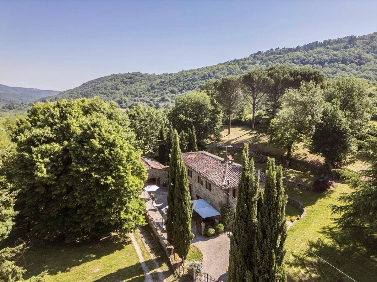 Luftaufnahme eines charmanten Anwesens mit Steinhaus, Pool und weitläufigem Garten in hügeliger Landschaft.
