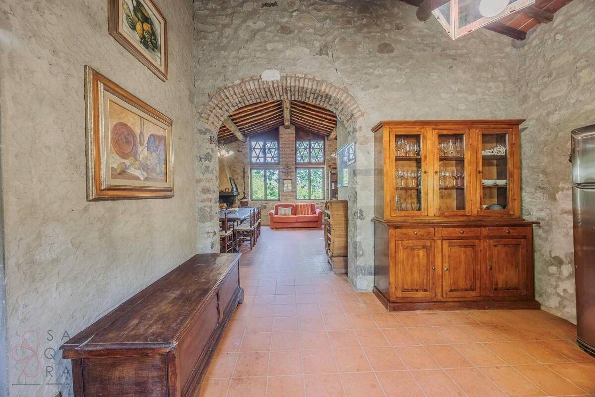 Rustikaler Wohnbereich mit Terrakottafliesen, Steinwänden und einem Durchgang zu einem weiteren Wohnraum.