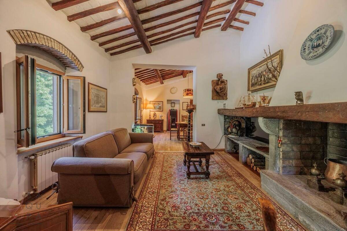 Helles Wohnzimmer mit bequemer Couch, Steinkamin und Blick auf den Garten durch große Fenster.