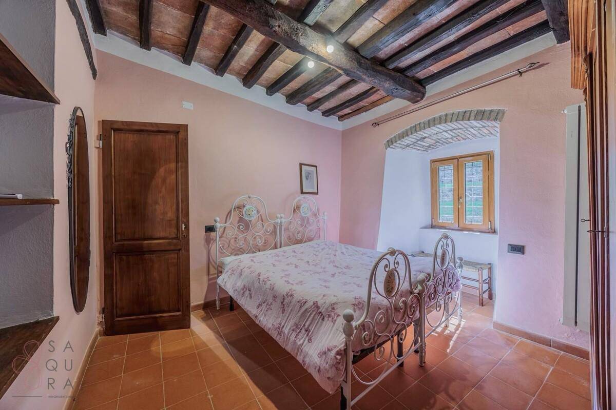 Romantisches Schlafzimmer mit Terrakottafliesen, Holzbalkendecke und einem Fenster mit Blick ins Grüne.