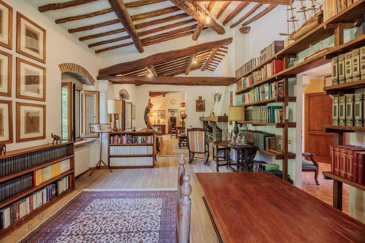 Großes Arbeitszimmer mit Holzboden, umfangreichen Bücherregalen und offenem Zugang zu einem weiteren Wohnbereich.