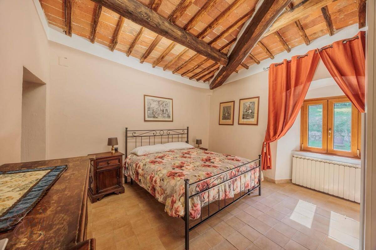 Rustikales Schlafzimmer mit Holzbalkendecke, Terrakottaboden und schmiedeeisernem Bett.
