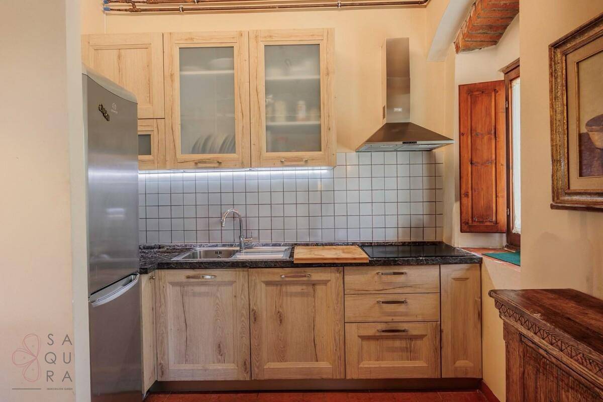 Helle Küche mit Holzschränken, Edelstahlgeräten und weiß gefliestem Spritzschutz.