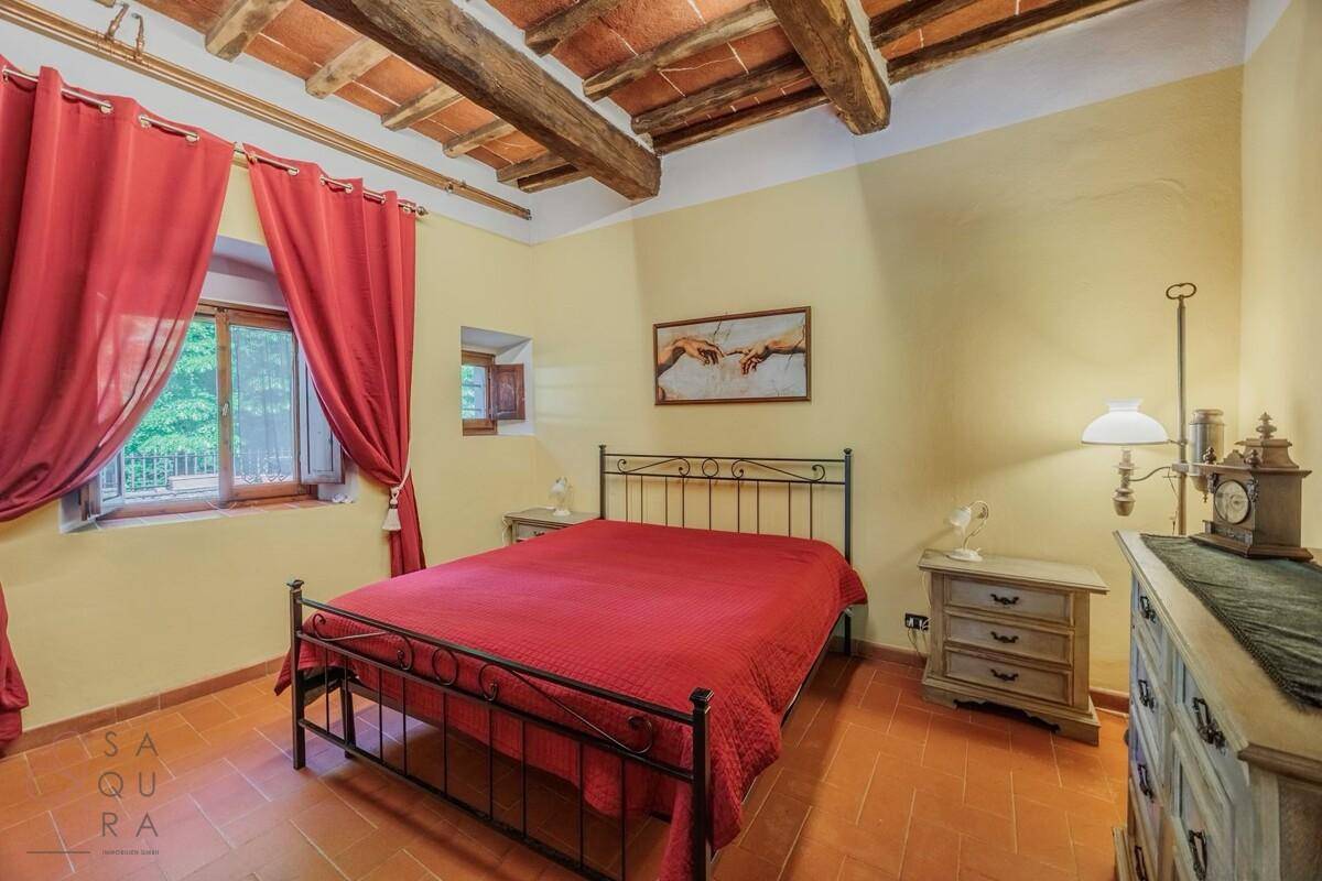 Gemütliches Schlafzimmer mit Terrakottaboden, Holzbalkendecke und Blick ins Grüne.