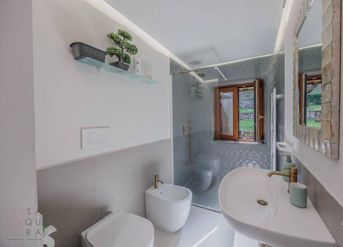 Modernes Badezimmer mit Dusche, Bidet und Fenster mit Blick ins Grüne.