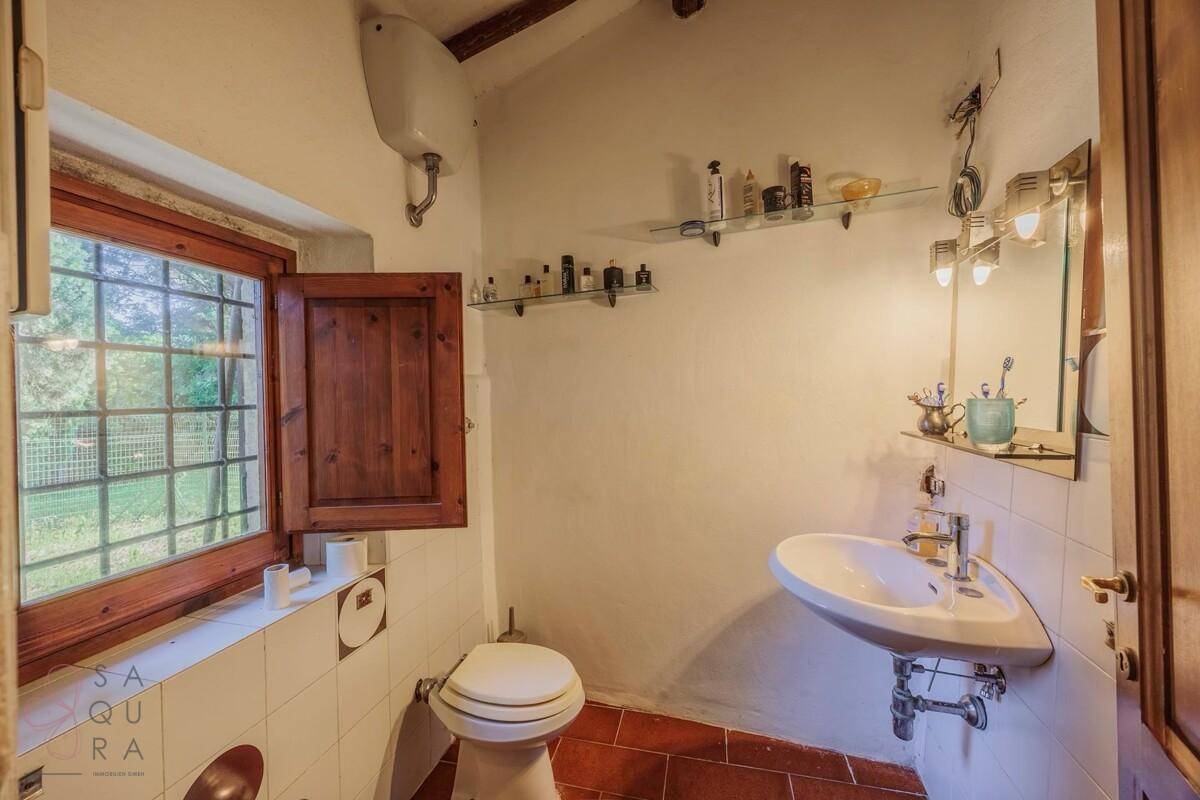 Kleines WC mit Fenster, Waschbecken und Terrakottaboden.