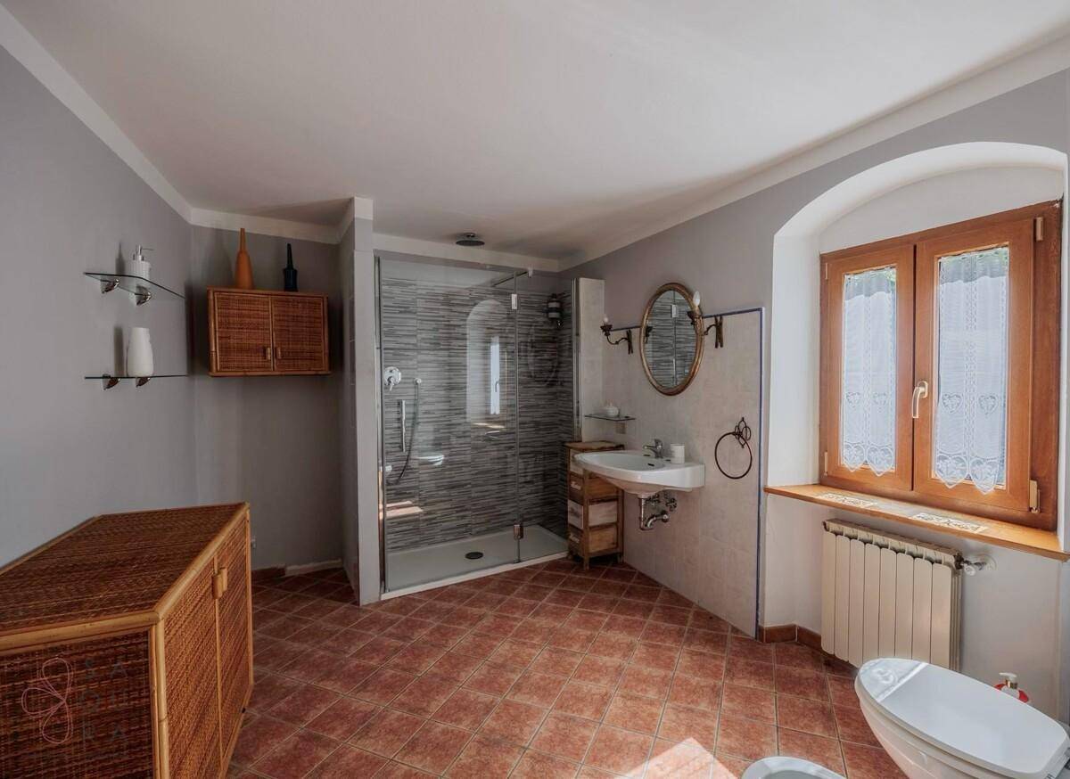 Geräumiges Badezimmer mit Dusche, Terrakottaboden und Fenster.