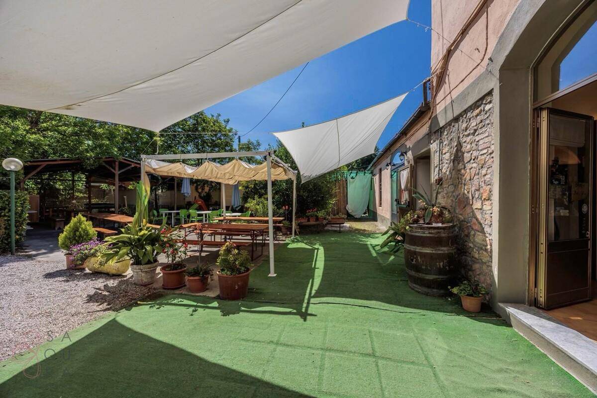 Großzügige Terrasse mit Sonnensegeln, Kunstrasen und rustikalen Sitzgelegenheiten.