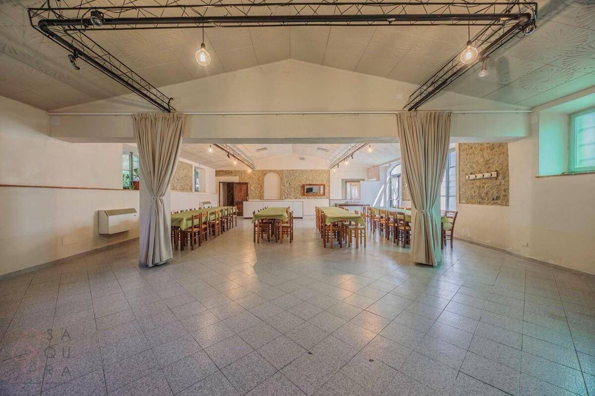 Geräumiger Speisesaal mit hohen Decken, Fliesenboden und vielen Tischen für Gäste.