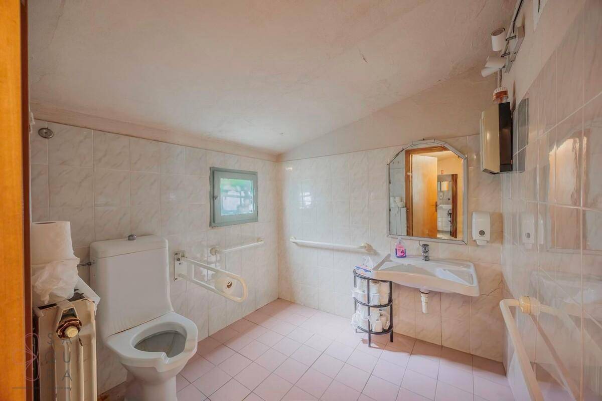Barrierefreies Badezimmer mit Haltegriffen, Fliesen und kleinem Fenster.