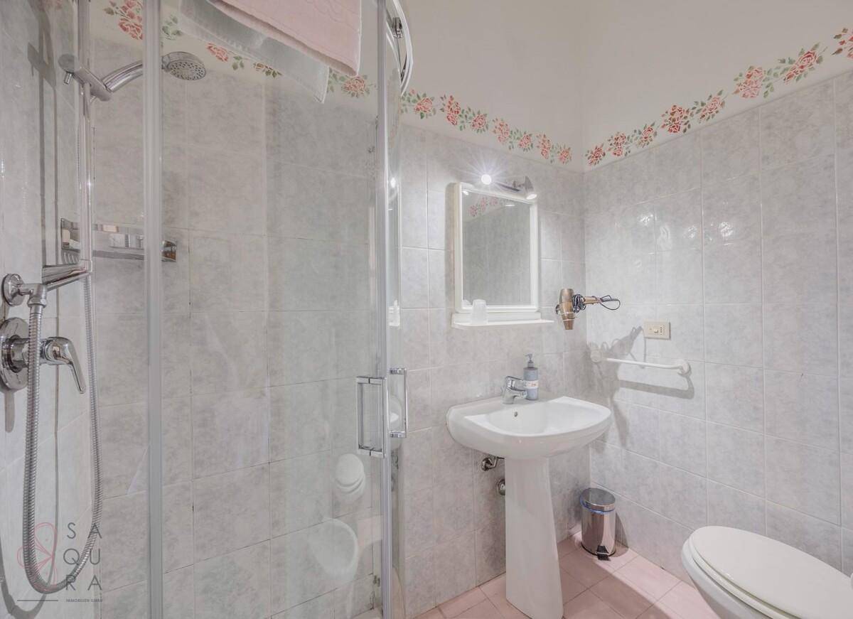 Funktionales Badezimmer mit Duschkabine, Standwaschbecken und hellen Fliesen.