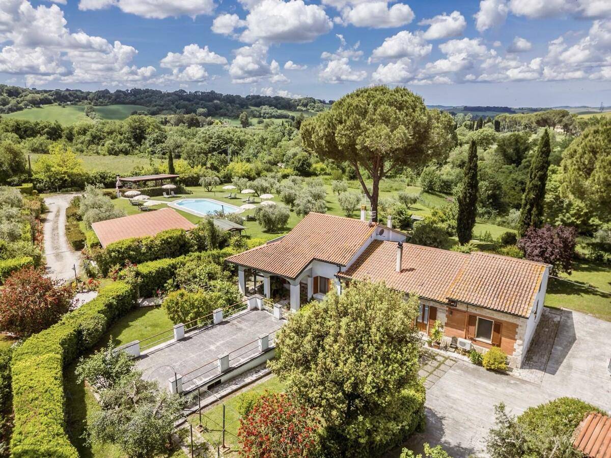 Haupthaus mit großer gepflasterter Terrasse und Blick auf den Poolbereich und die Landschaft.