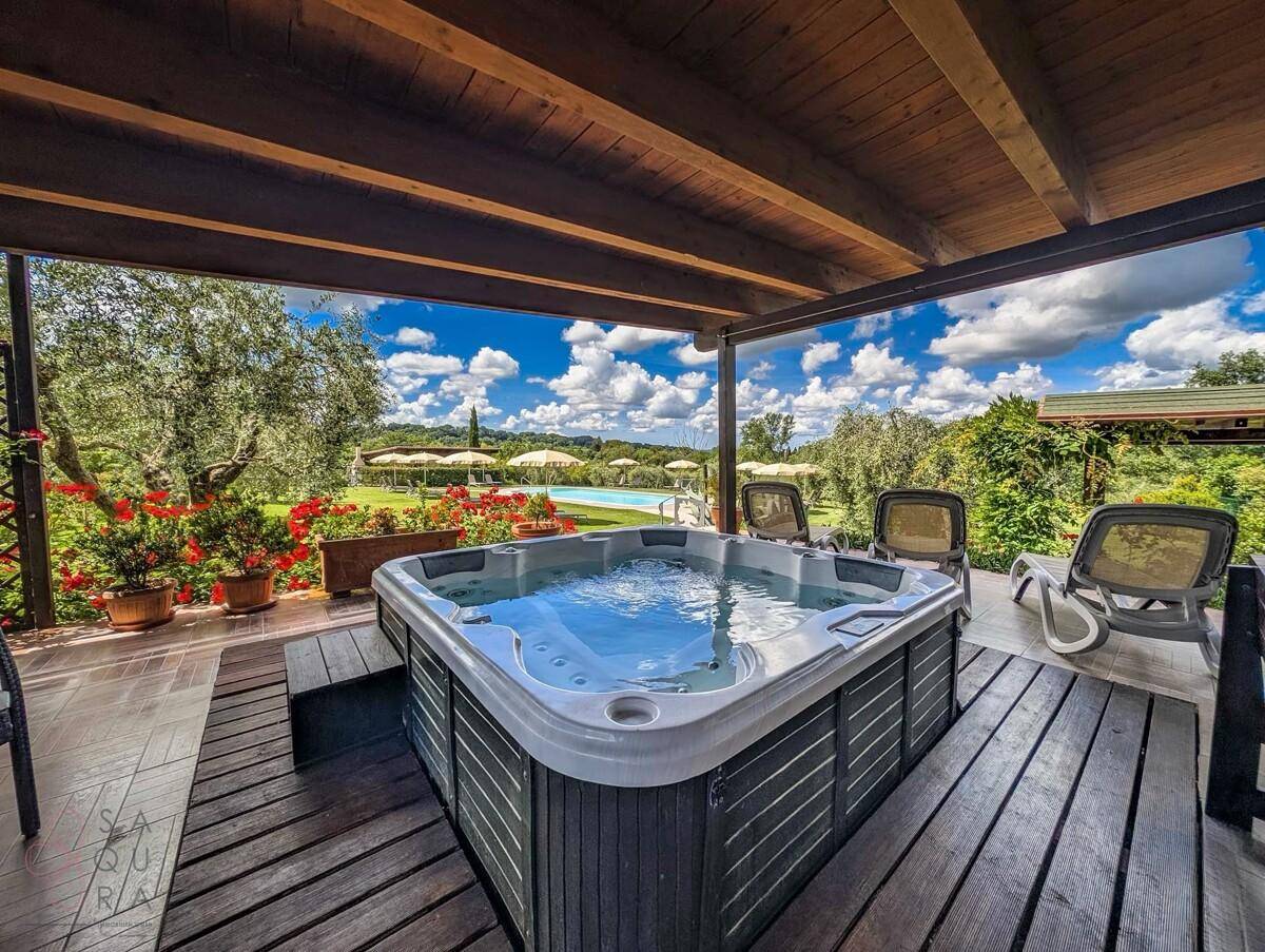 Überdachter Außenbereich mit Whirlpool und Holzterrasse, mit Blick auf den Pool und die Landschaft.