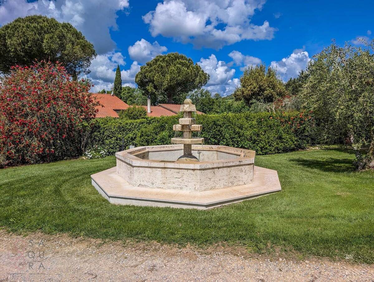 Dekorativer mehrstufiger Steinbrunnen in einem gepflegten Rasenbereich, umgeben von Hecken.