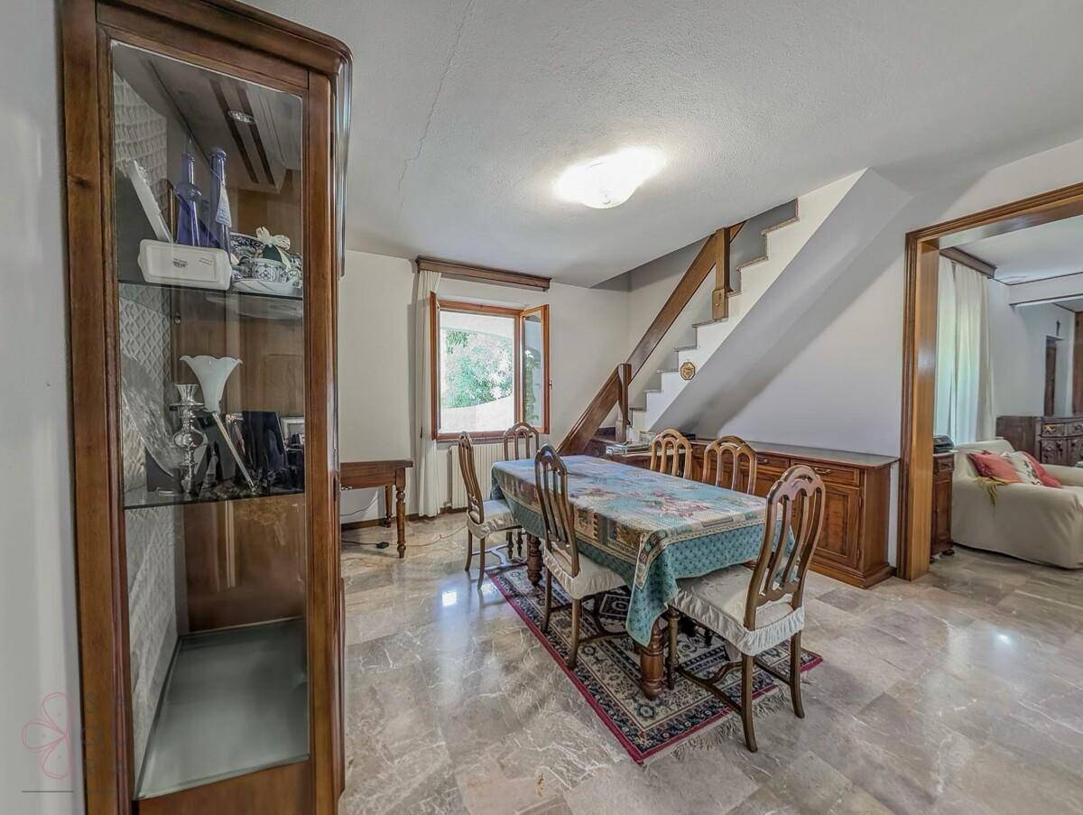 Klassisches Esszimmer mit Holztisch, Vitrine und Marmorboden, mit Treppe im Hintergrund.