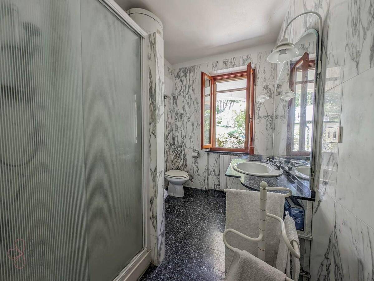 Badezimmer mit Marmorwänden, Duschkabine und Fenster, das Tageslicht hereinlässt.