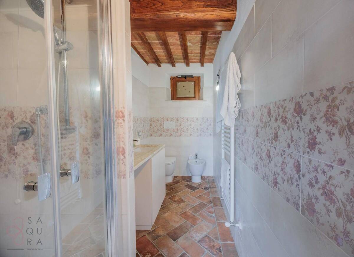 Badezimmer mit Dusche, Bidet, Terrakottaboden und floral gemusterten Wandfliesen.