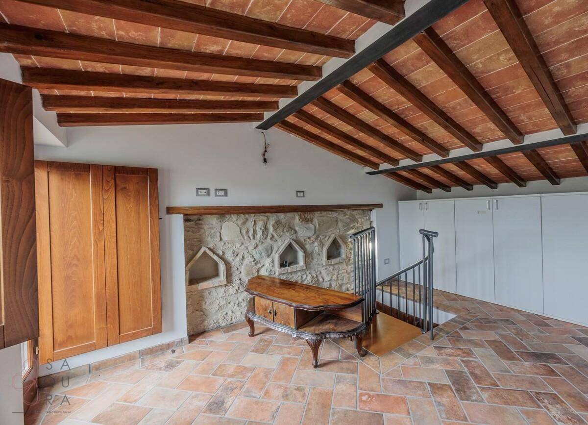 Geräumiger Raum mit Terrakottaboden, freiliegenden Holzbalken und einer dekorativen Steinwand.