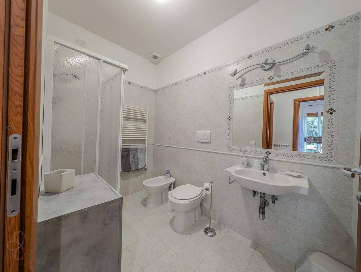 Helles Badezimmer mit weißen Fliesen, Duschkabine, Bidet und beheiztem Handtuchhalter.