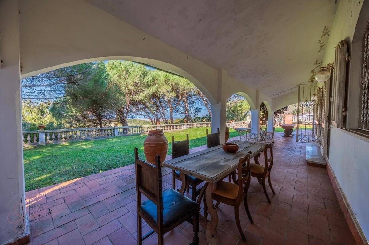 Blick von der überdachten Loggia mit Esstisch auf den Garten und das ferne Meer.