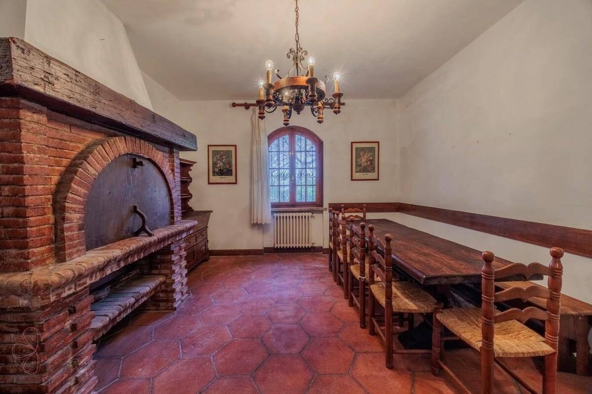 Rustikaler Essbereich mit großem gemauerten Kamin, langem Holztisch und Terrakottaboden.