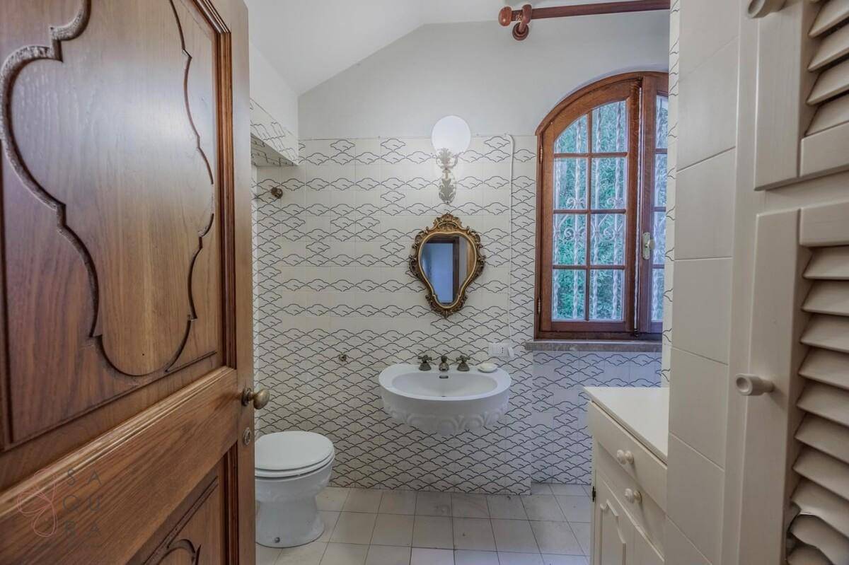 Badezimmer mit gemusterten Fliesen, Einzelwaschbecken, Toilette und Fenster.